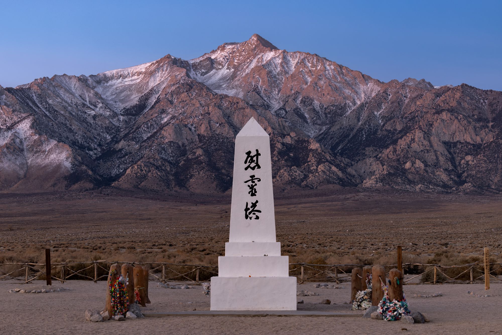 Vibrant sunrise view of the white monument (the Kanji characters literally mean soul consoling tower, 慰霊塔) at Manzanar Cemetery, with Mount Williamson and the Eastern Sierra seen in the background being touched by the first soft pink sunlight of the new day.