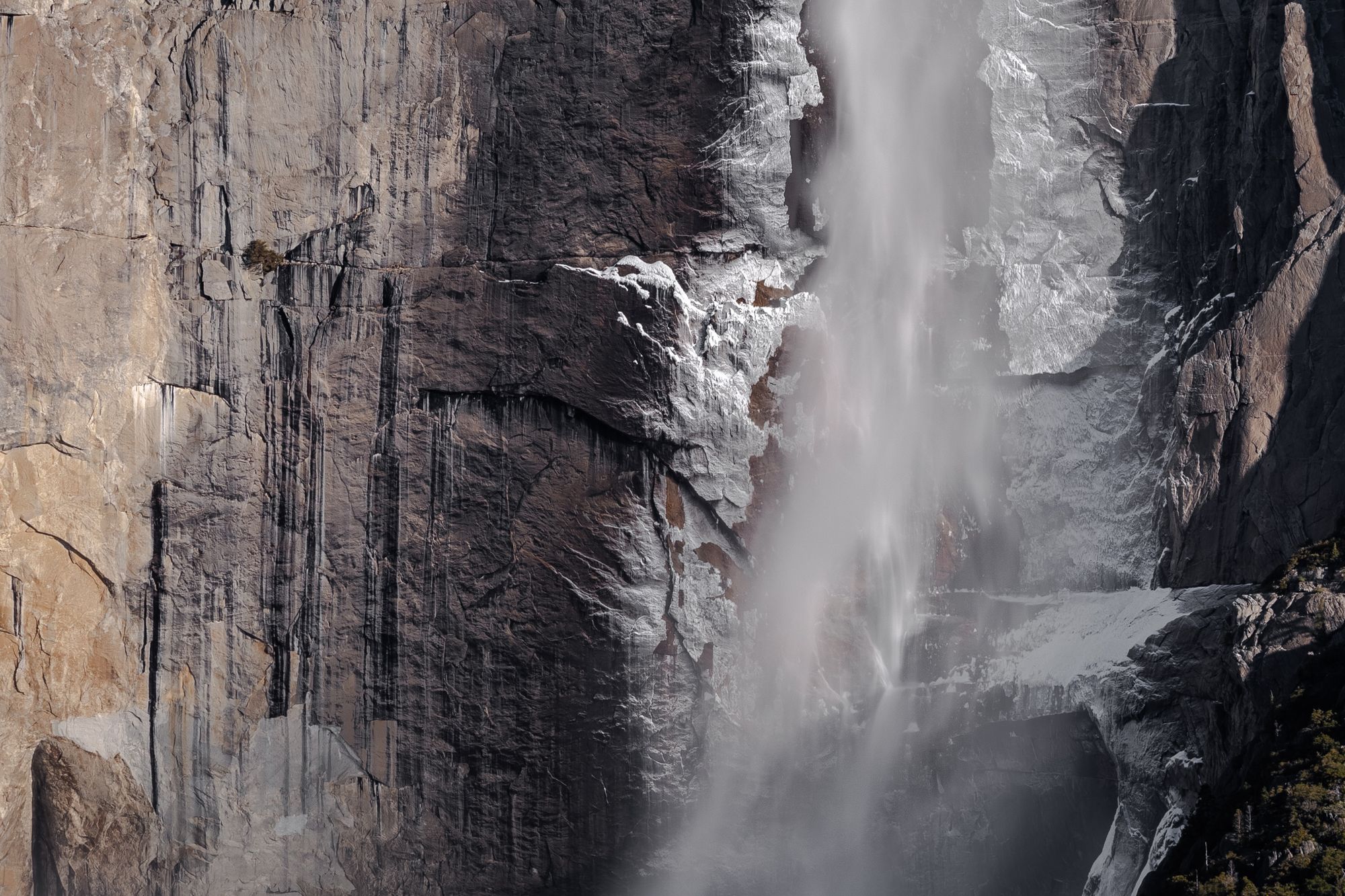 Zoomed-in view of Yosemite Falls on the right, and on the left a bare rock face covered with stripes of black lichens.